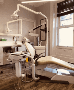 News 7 Voyagerili dental chair with overhead light in bright dental clinic room, brushed wood flooring, window with blinds, and framed certificates on wall for Hewett's Dental services in Brighouse, Huddersfield, Halifax, Bradford.