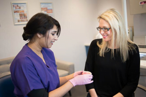 News 9 A woman in purple dental scrubs showing a dental model to a smiling female patient wearing glasses in a modern dental clinic.